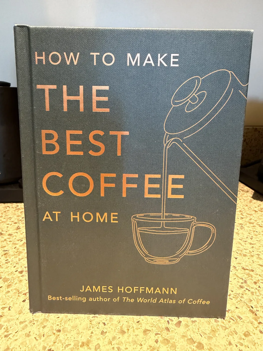 How to Make the Best Coffee at Home by James Hoffmann, a dark grey hardback with an orange line drawing of a kettle pouring into a cup, standing on a kitchen counter.