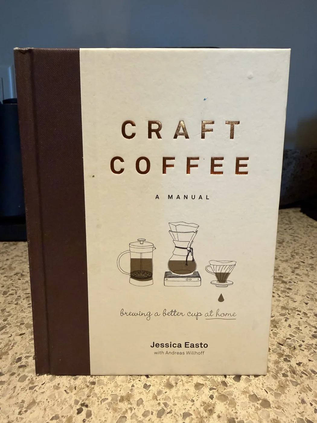 Craft Coffee: A Manual by Jessica Easto with Andreas Willhoff, a cream and brown hardback with line drawings of a French press, a Chemex on a scale, and a cone dripper.