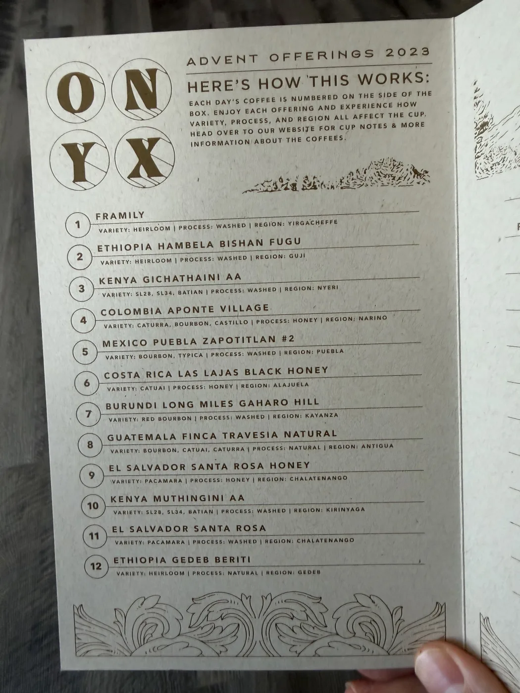 A printed card headed ADVENT OFFERINGS 2023 with the ONYX logo in four circles, listing coffees 1 through 12. Each line gives a coffee name in capitals with variety, process and region printed beneath it in smaller type.