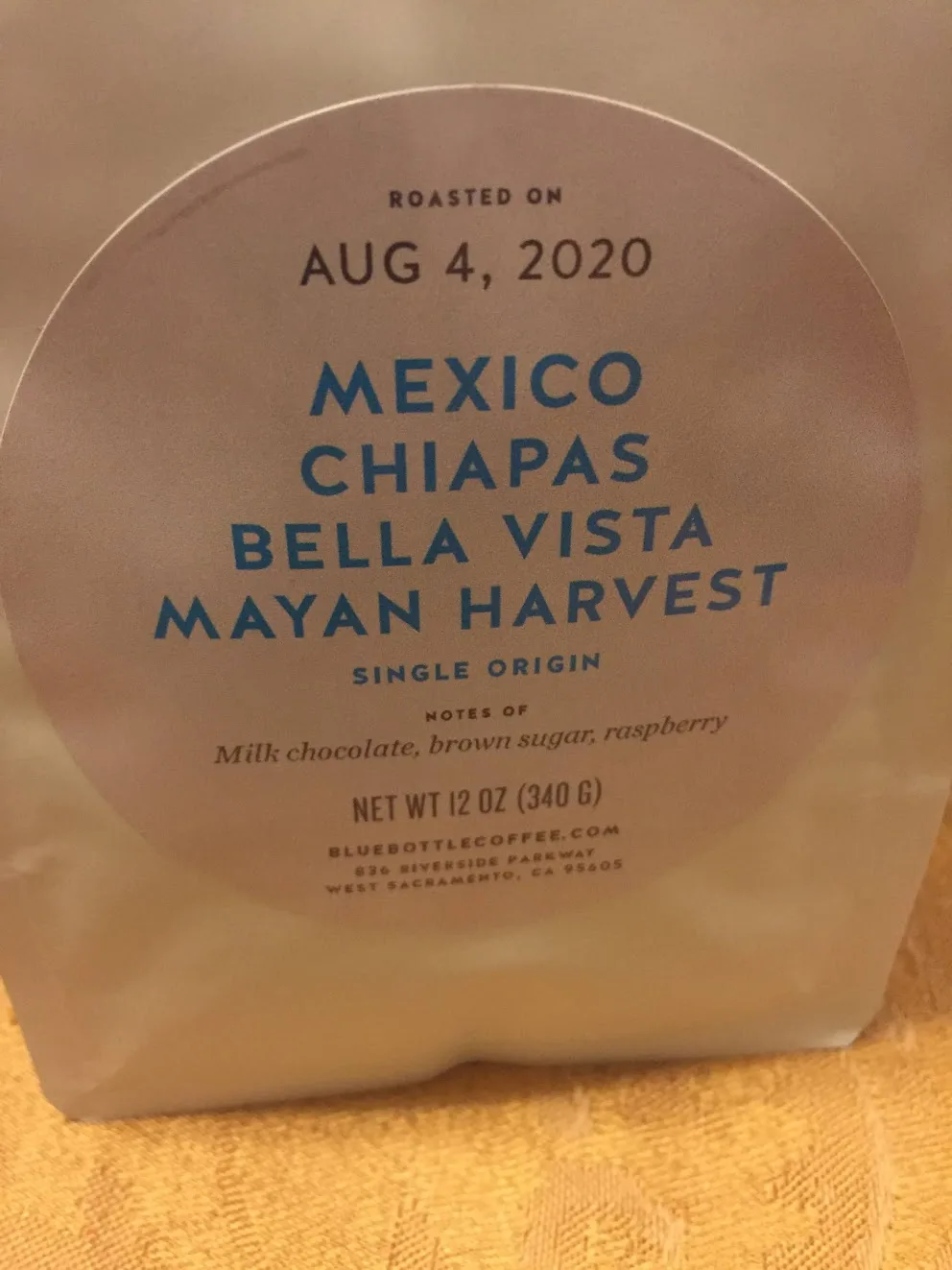 A Blue Bottle bag with a large circular label reading ROASTED ON AUG 4, 2020, MEXICO CHIAPAS BELLA VISTA MAYAN HARVEST, SINGLE ORIGIN, notes of milk chocolate, brown sugar, raspberry, net weight 12 oz, and the address 836 RIVERSIDE PARKWAY, WEST SACRAMENTO, CA 95605.