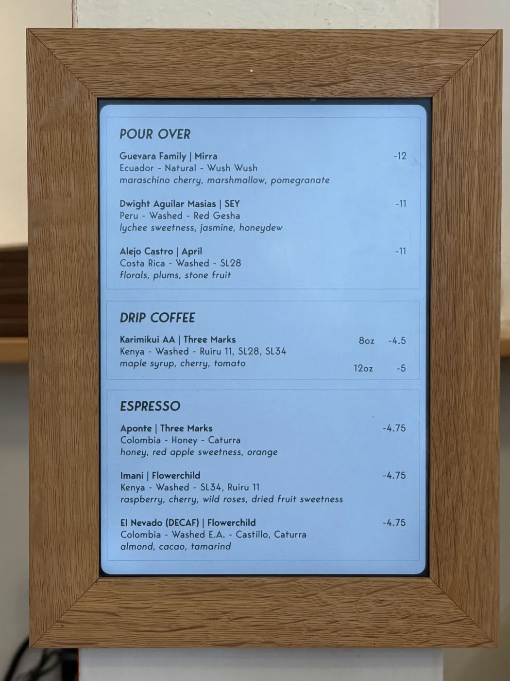 Homage Coffee's pour-over menu board listing the Guevara Family Wush Wush from Ecuador roasted by Mirra with maraschino cherry, marshmallow and pomegranate at twelve dollars, alongside a washed red Gesha from Peru roasted by SEY and a washed SL28 from Costa Rica roasted by April.